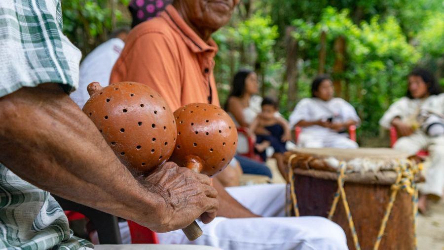 Manos de un músico mayor sostienen maracas junto a un tambor, durante un encuentro de cumbia