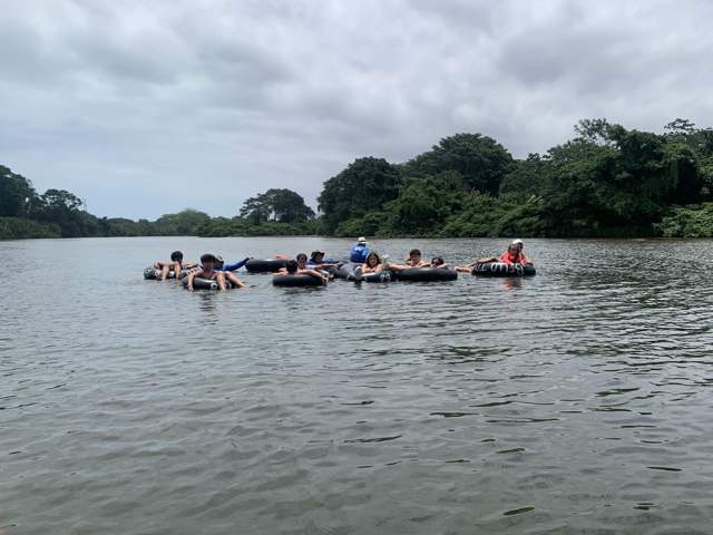 Grupo de viajeros flotando en neumáticos sobre un río ancho bordeado de selva
