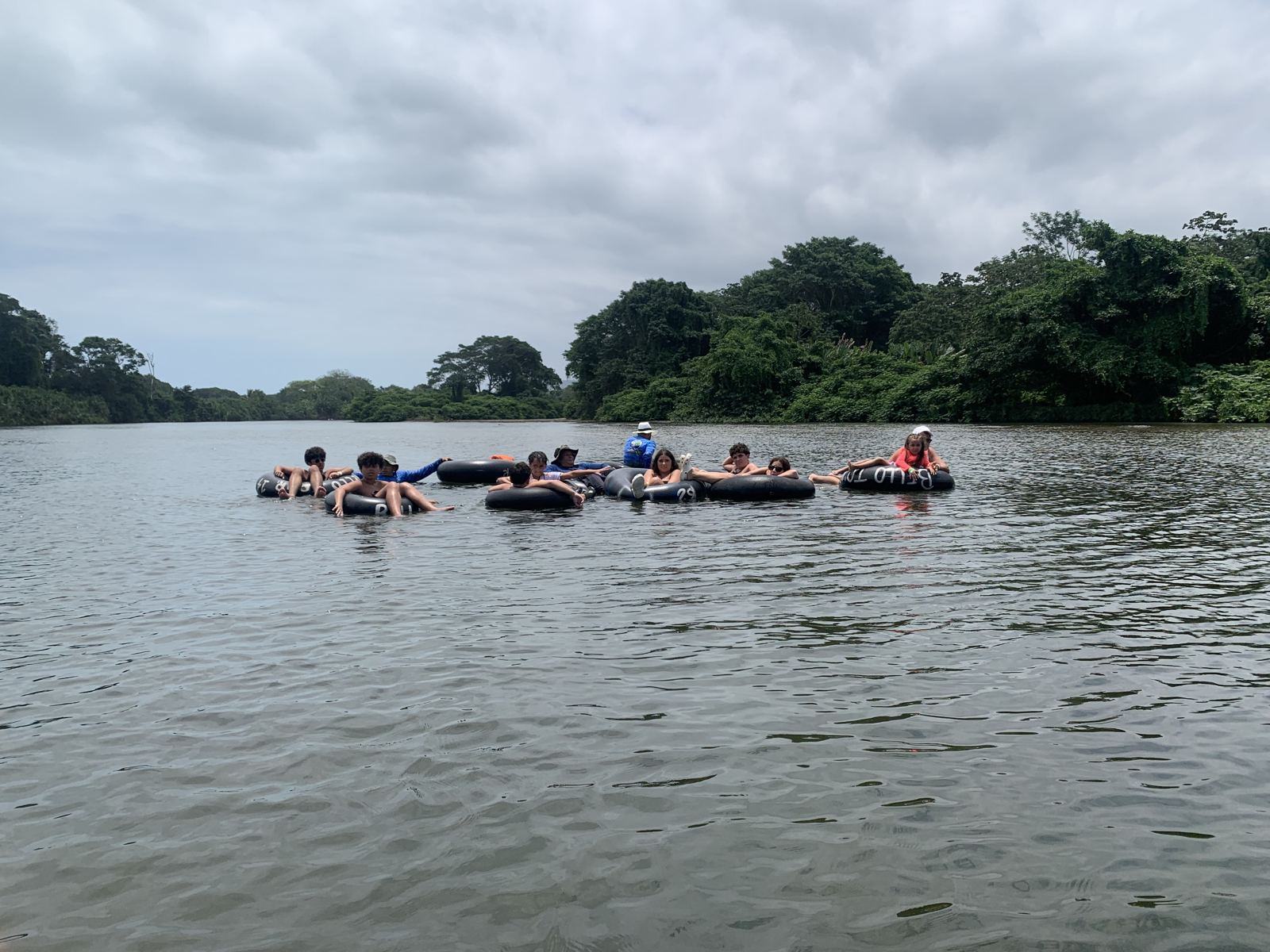 Grupo de viajeros flotando en neumáticos sobre un río ancho bordeado de selva