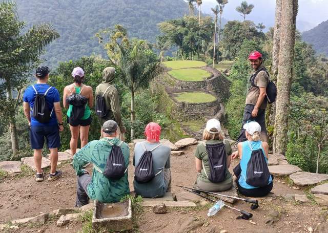 Caminantes descansan frente a las terrazas circulares de piedra de Teyuna, rodeadas de selva y palmas